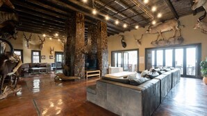 A spacious living room with a stone fireplace, leather sofa, and mounted animal heads on the walls. - Humdani Game Lodge (Beestekraal)