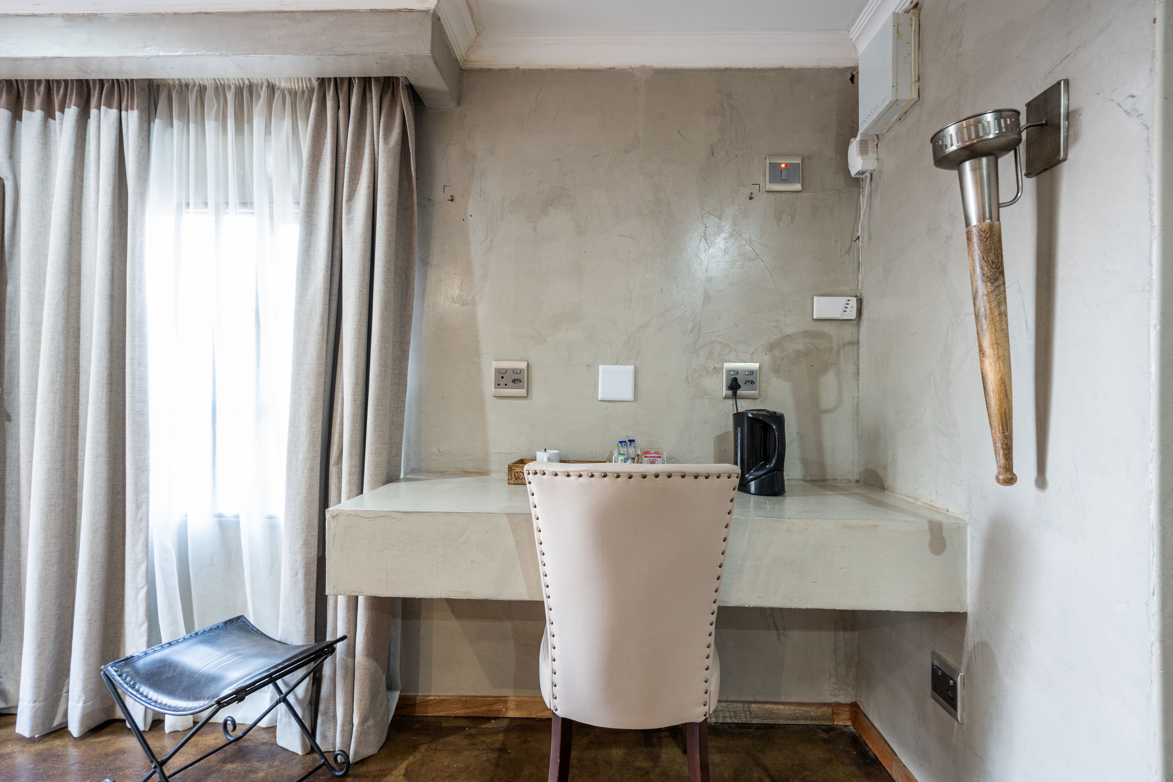 Una habitación con un escritorio, una silla, una cafetera y un martillo en la pared.