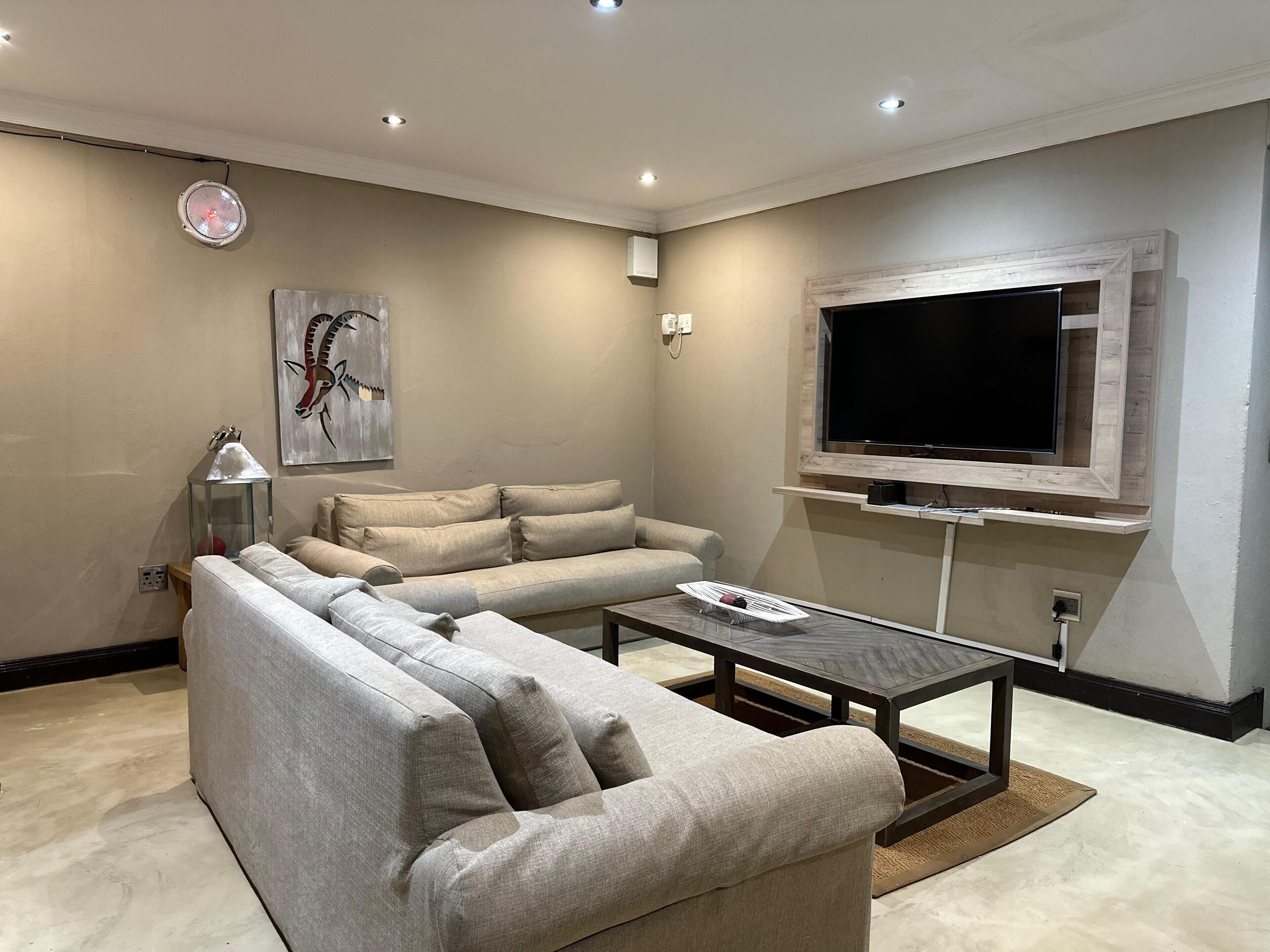 A modern living room with a sectional sofa, a coffee table, a flat-screen TV mounted on the wall, and a decorative lamp.