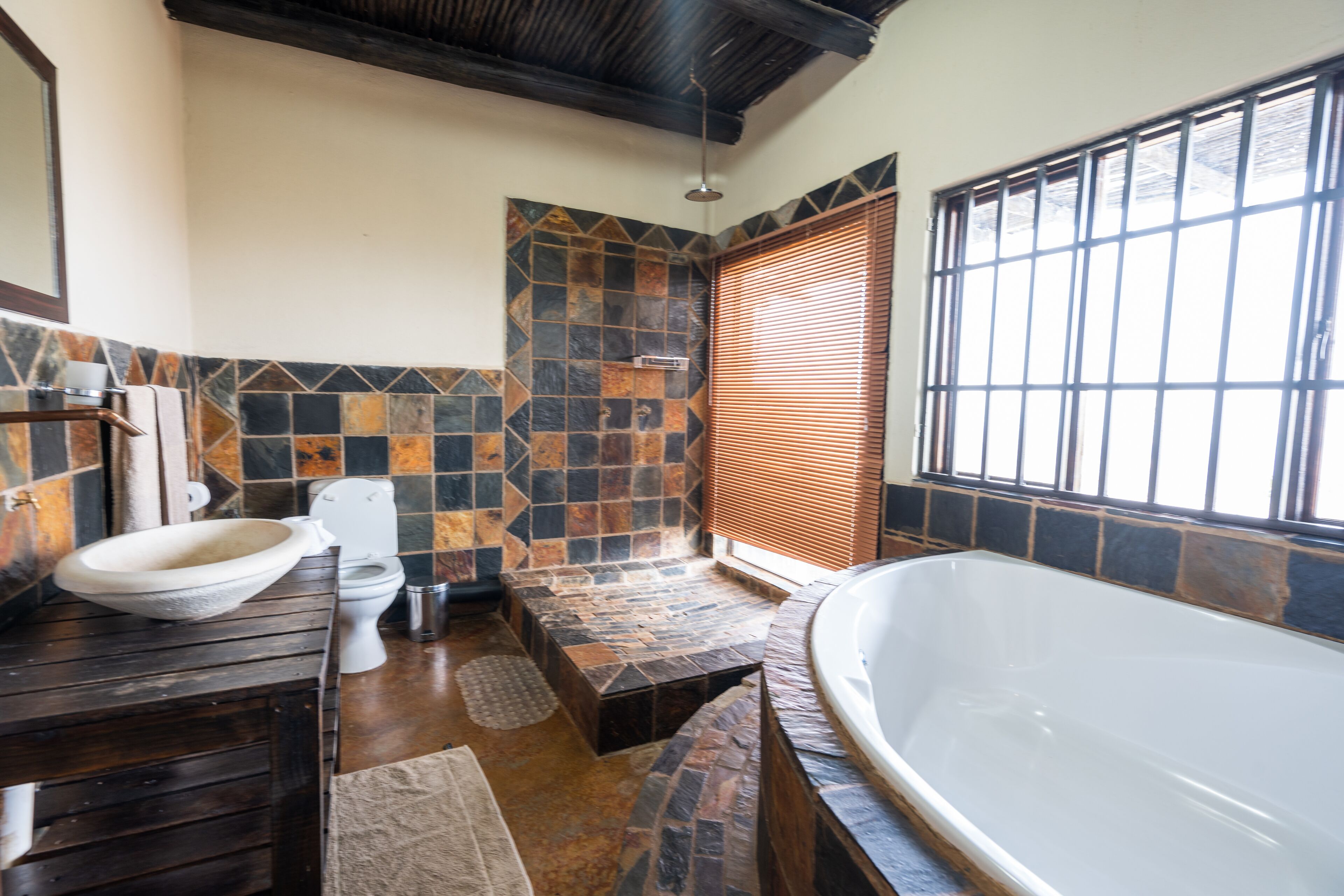 A bathroom with a stone-tiled shower, a bathtub, and a toilet.