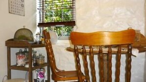 A dining area with a wooden chair and table, a window with blinds, and a shelf with various items. - Brim Brim Gardens (Buninyong)