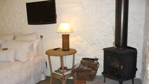 A cozy room with a white bed, a small round table with a lamp, and a black wood-burning stove. - Brim Brim Gardens (Buninyong)