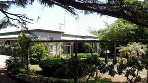 A building with a white roof and a covered porch, surrounded by well-maintained gardens and trees. - Brim Brim Gardens (Buninyong)