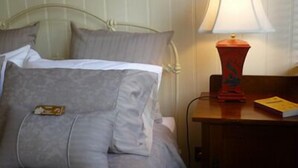 A bed with a gray duvet and pillows, a red lamp on a wooden nightstand, and a book on the nightstand. - Brim Brim Gardens (Buninyong)