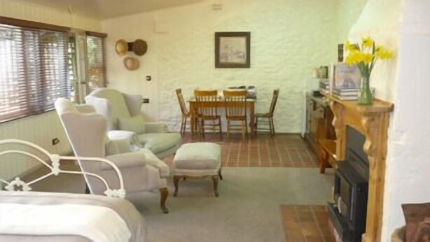 A cozy room with a bed, a chair, a table, and a fireplace. - Brim Brim Gardens (Buninyong)