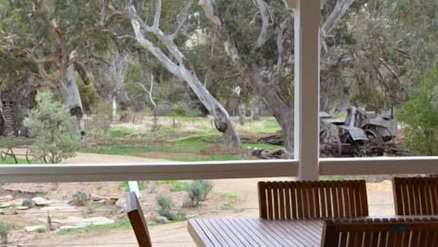 A view from a window with a wooden table and chairs, overlooking a natural landscape with trees and a dirt path. - Brooklyn Farm Bed and Breakfast (Myponga Beach)
