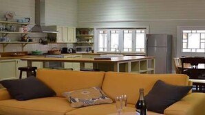 A spacious living room with a yellow sofa, a dining area with a wooden table and chairs, and a kitchen with white cabinets and a refrigerator. - Brooklyn Farm Bed and Breakfast (Myponga Beach)