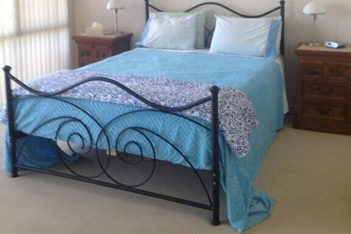 A bedroom with a bed, two bedside tables, a nightstand, a wall-mounted air conditioner, and a window with blinds.
