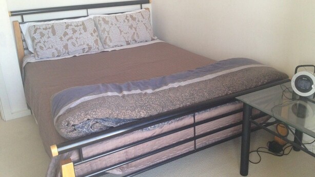 A bed with a mattress, pillows, and a glass table with a clock. - Christies No 1 Esplanade (Christies Beach)