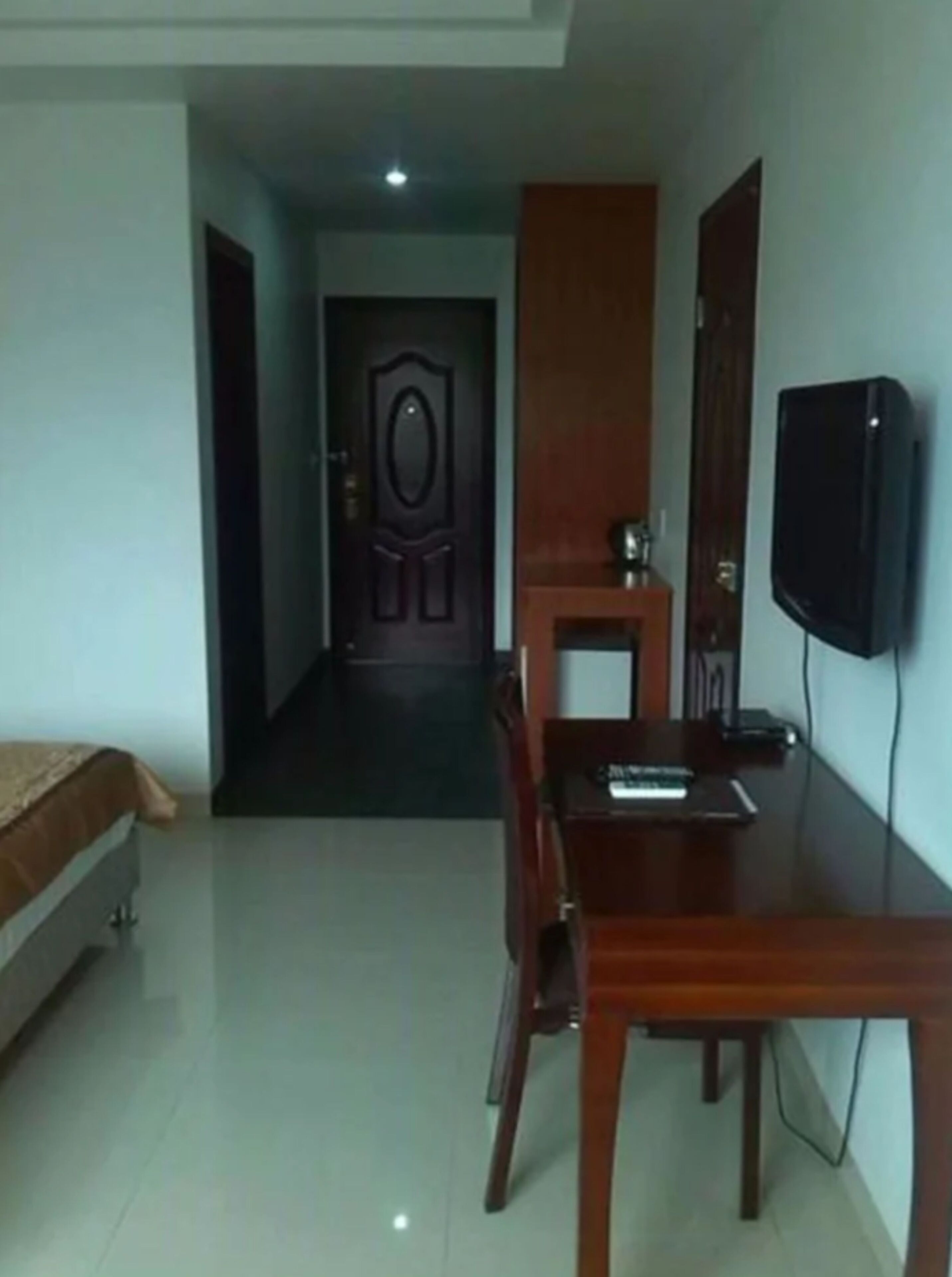 A hotel room with a bed, a desk, a chair, a television, and a door.