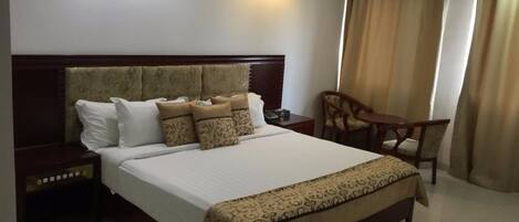 A hotel room with a large bed, a bedside table, a chair, and a desk.