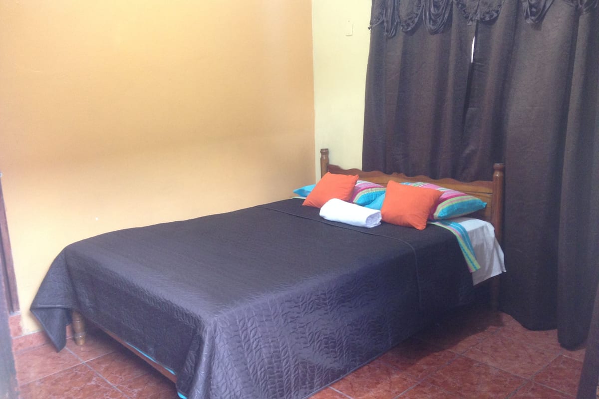 A single bed with a dark bedspread, two pillows, and a rolled towel.