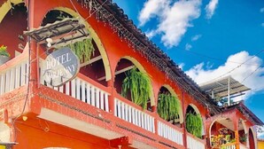 A hotel with a red facade, multiple balconies with hanging plants, and a 'Welcome' sign at the entrance. - Hotel Marjenny (Copan Ruinas)