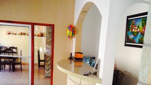 A spacious living area with a curved stone counter, a dining table with chairs, and a kitchen visible through an open door. - Hotel Marjenny (Copan Ruinas)
