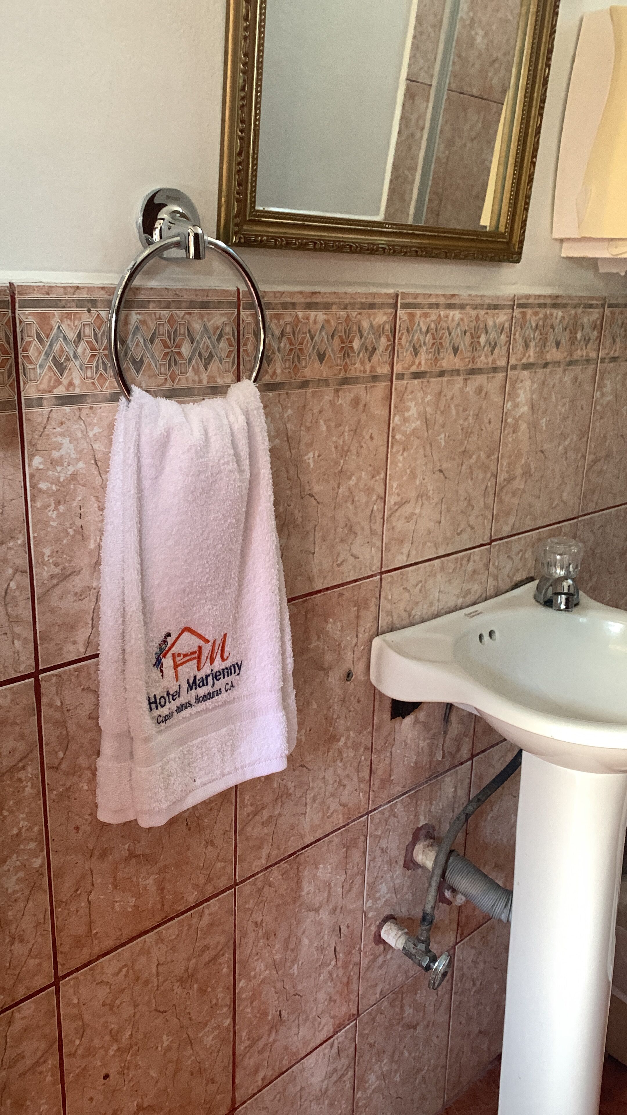Un baño con un lavamanos blanco, una toalla colgada en un perchero metálico y un salpicadero decorativo de azulejos.