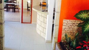 A spacious room with a tiled floor, a stone wall, and a colorful plant arrangement. - Hotel Marjenny (Copan Ruinas)