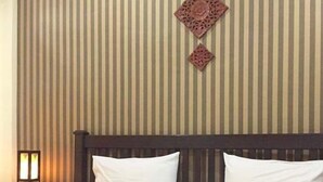 Habitación de hotel con papel tapiz a rayas, cabecera de madera, ropa de cama blanca y almohada decorativa.