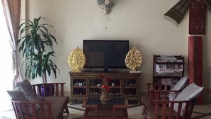 Una sala de estar con televisor, dos sillas de madera, una mesa de centro, una planta en maceta y una estantería.