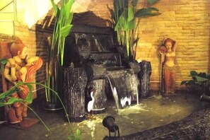 A stone fountain with statues, surrounded by plants. - Domon Hotel (Vientiane)