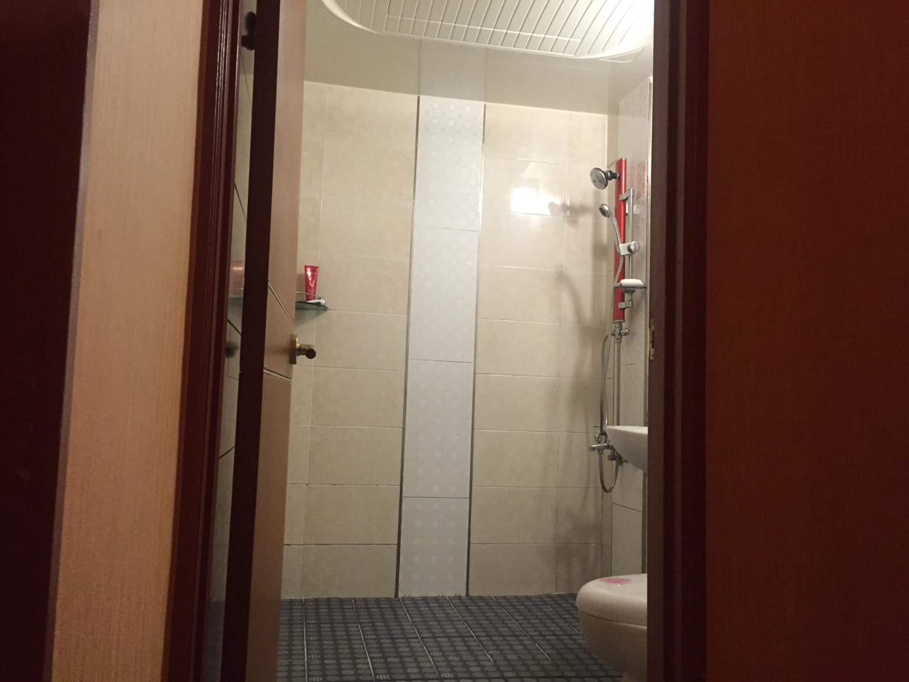 A bathroom with a shower, toilet, and a small shelf with a cup.