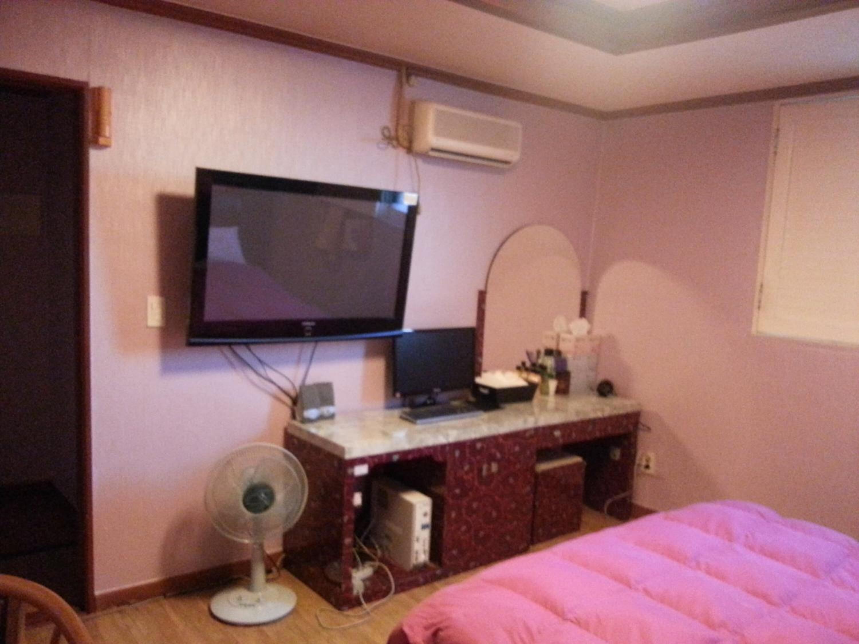 A hotel room with a bed, a desk with a computer, a television, and a fan.
