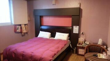 Een hotelkamer met een bed, bureau, stoel en een raam met jaloezieën.