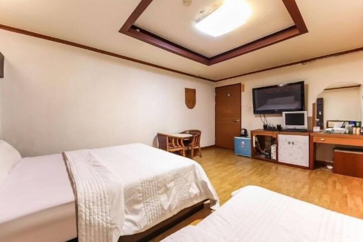 Habitación de hotel con dos camas, un escritorio con computadora, televisor y una pequeña zona de estar.
