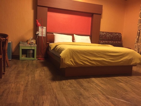 A hotel room with a wooden bed, a nightstand, a red lamp, and a small green cabinet.