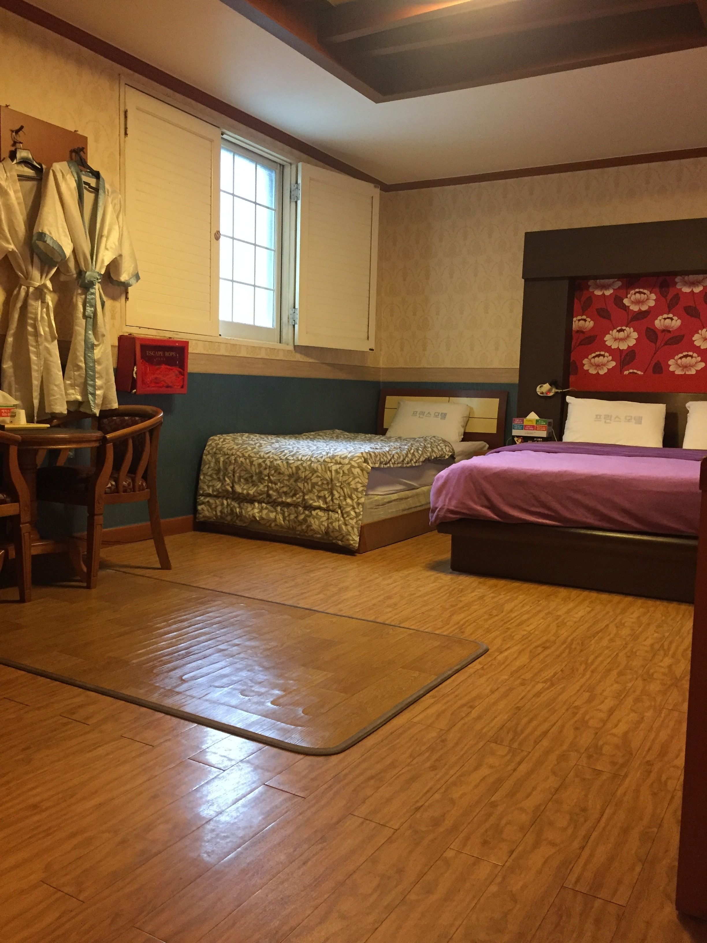 Un dormitorio con suelo de madera, una cama con colcha estampada, una silla, un escritorio y una ventana con vistas al exterior.