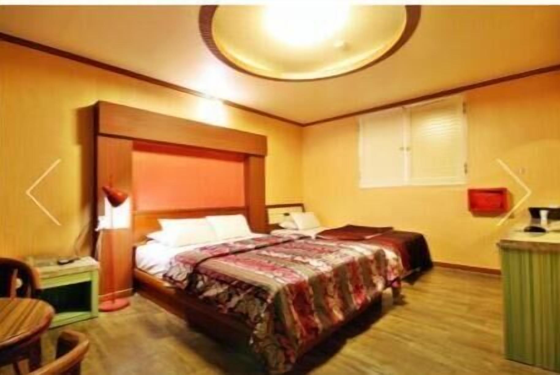 A bedroom with a bed, bedside table, lamp, and a small cabinet.