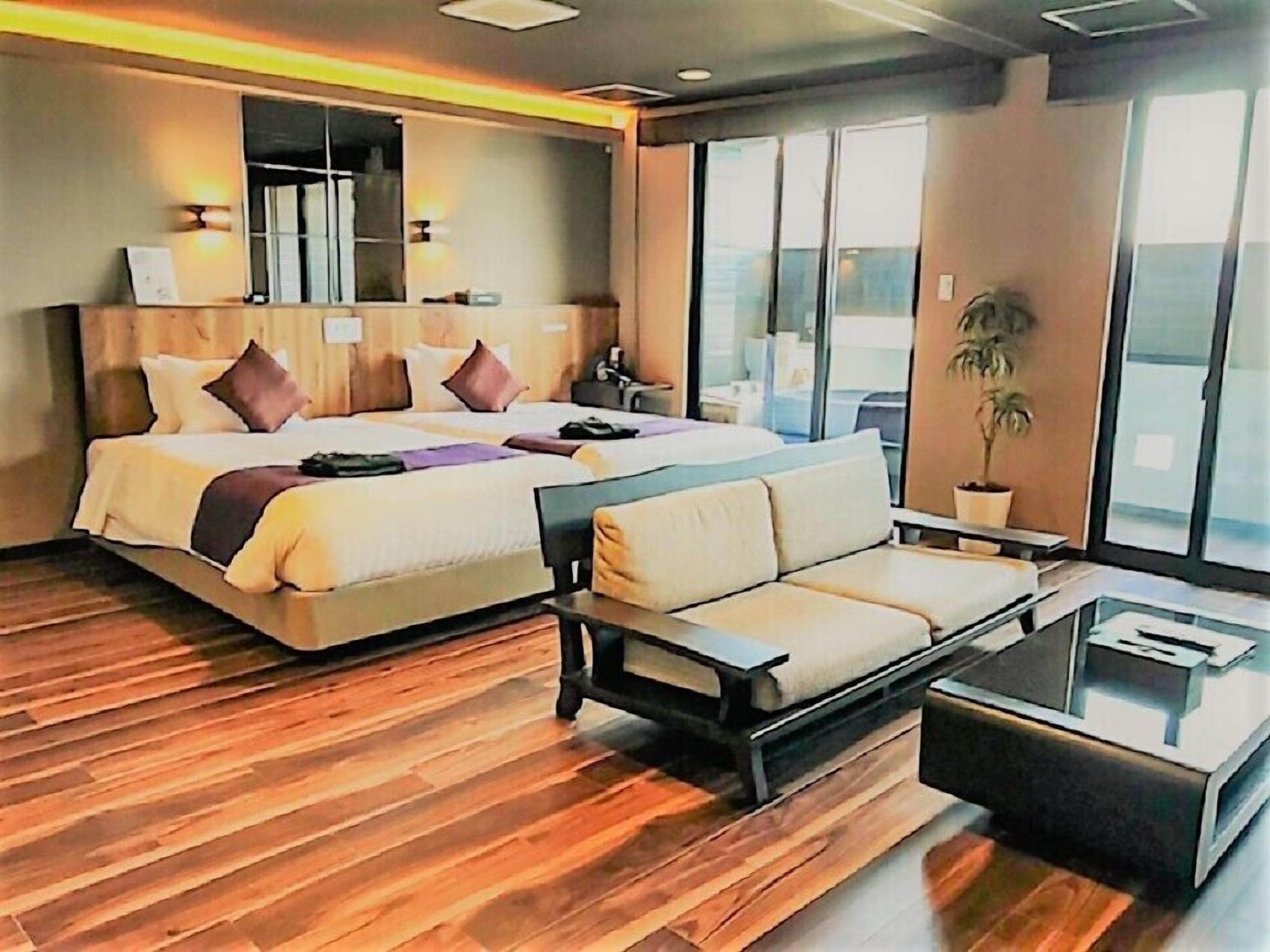 A modern hotel room with a large bed, a sofa, a coffee table, and a potted plant.