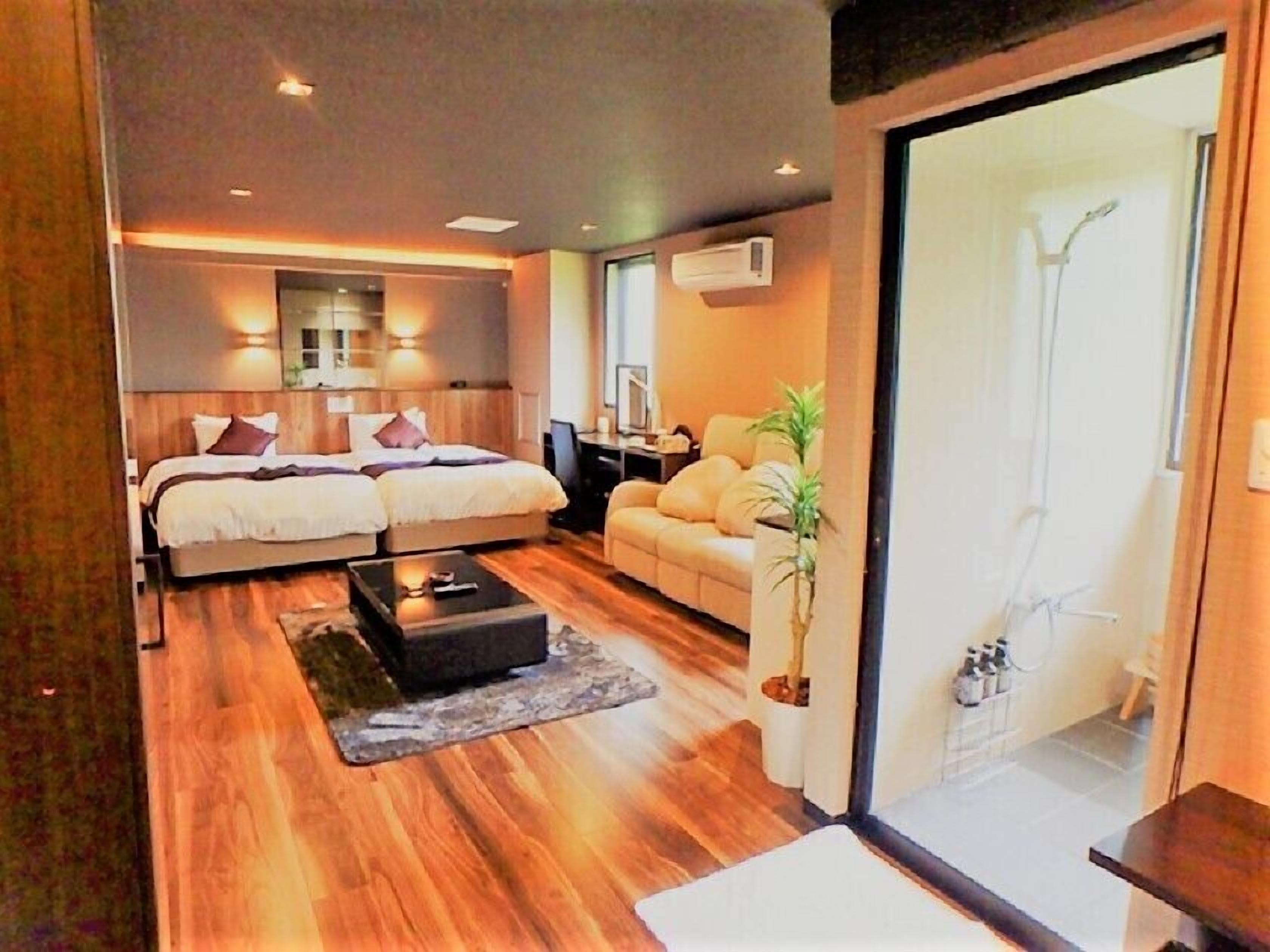 A modern bedroom with a double bed, a sofa, a coffee table, and a potted plant.