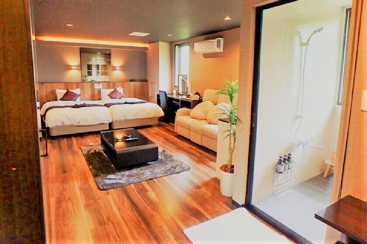 Een moderne slaapkamer met een tweepersoonsbed, een slaapbank, een bijzettafeltje en een potplant.