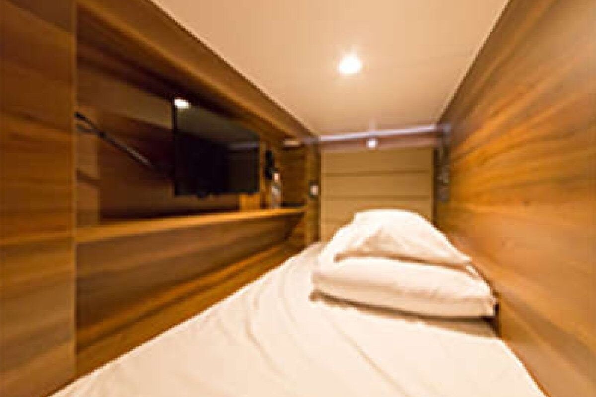 A narrow room with a bed, wooden paneling, a television, and a ceiling light.