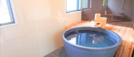 A room with a large black bathtub, wooden flooring, and a window providing natural light.
