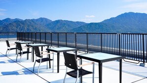 Een terras met tafels en stoelen, met uitzicht op een bergachtig landschap.