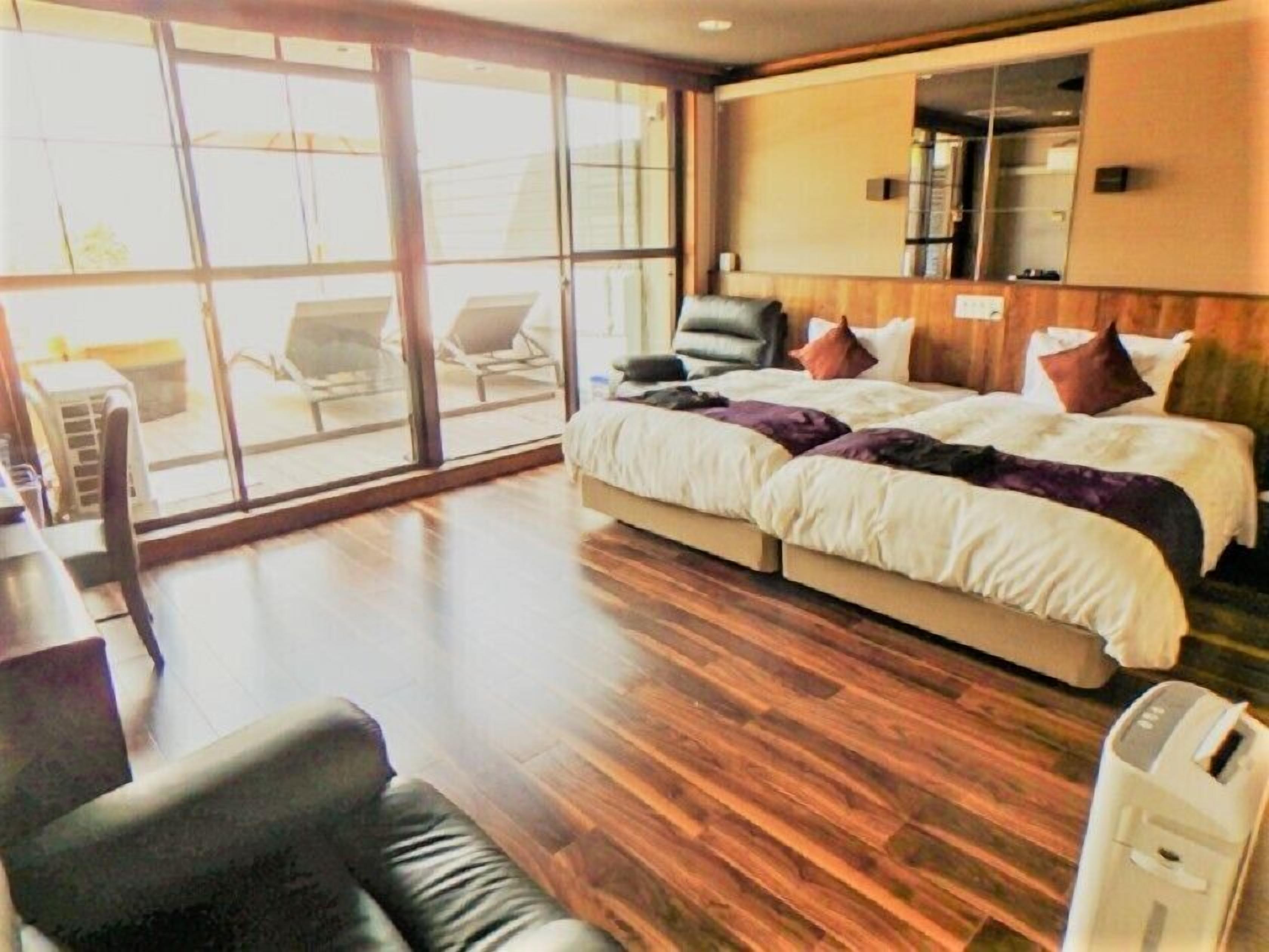 A hotel room with a large bed, a sofa, a desk, and a view through large windows.
