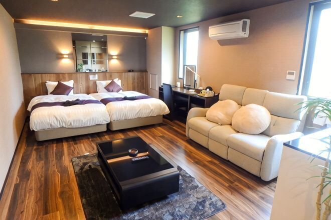 A hotel room with a double bed, a sofa, a coffee table, and a large window.
