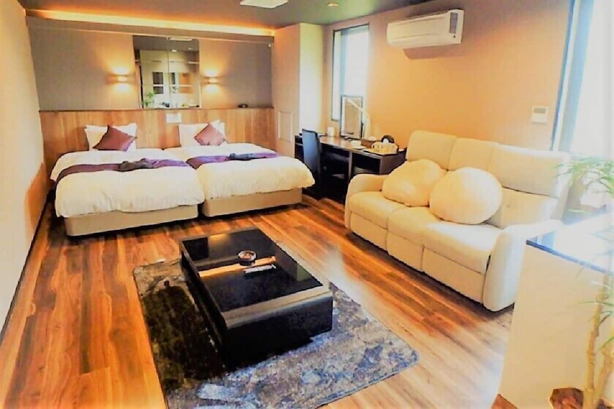 Een moderne hotelkamer met twee bedden, een bank, een bureau en een groot raam.