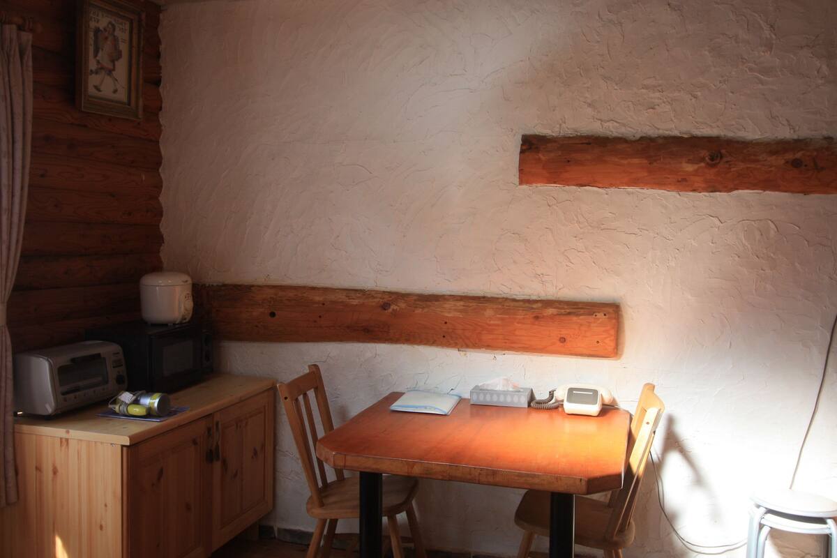 Ein Holzblockhaus-Interieur mit Esstisch, Stühlen, einer Mikrowelle, einem Toaster und einem kleinen Schrank.