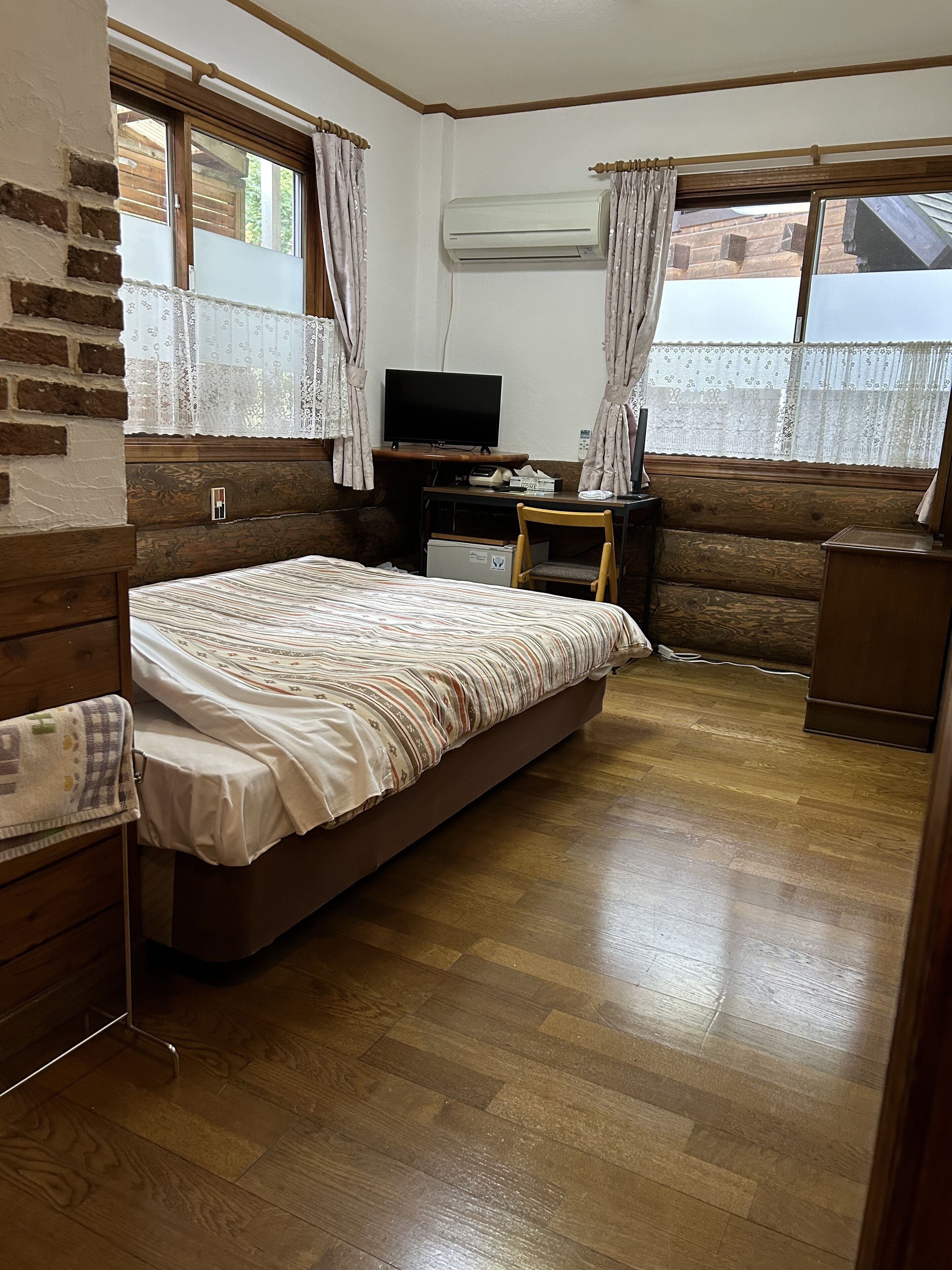 Ein Schlafzimmer mit Bett, Schreibtisch, Fernseher und Klimaanlage.