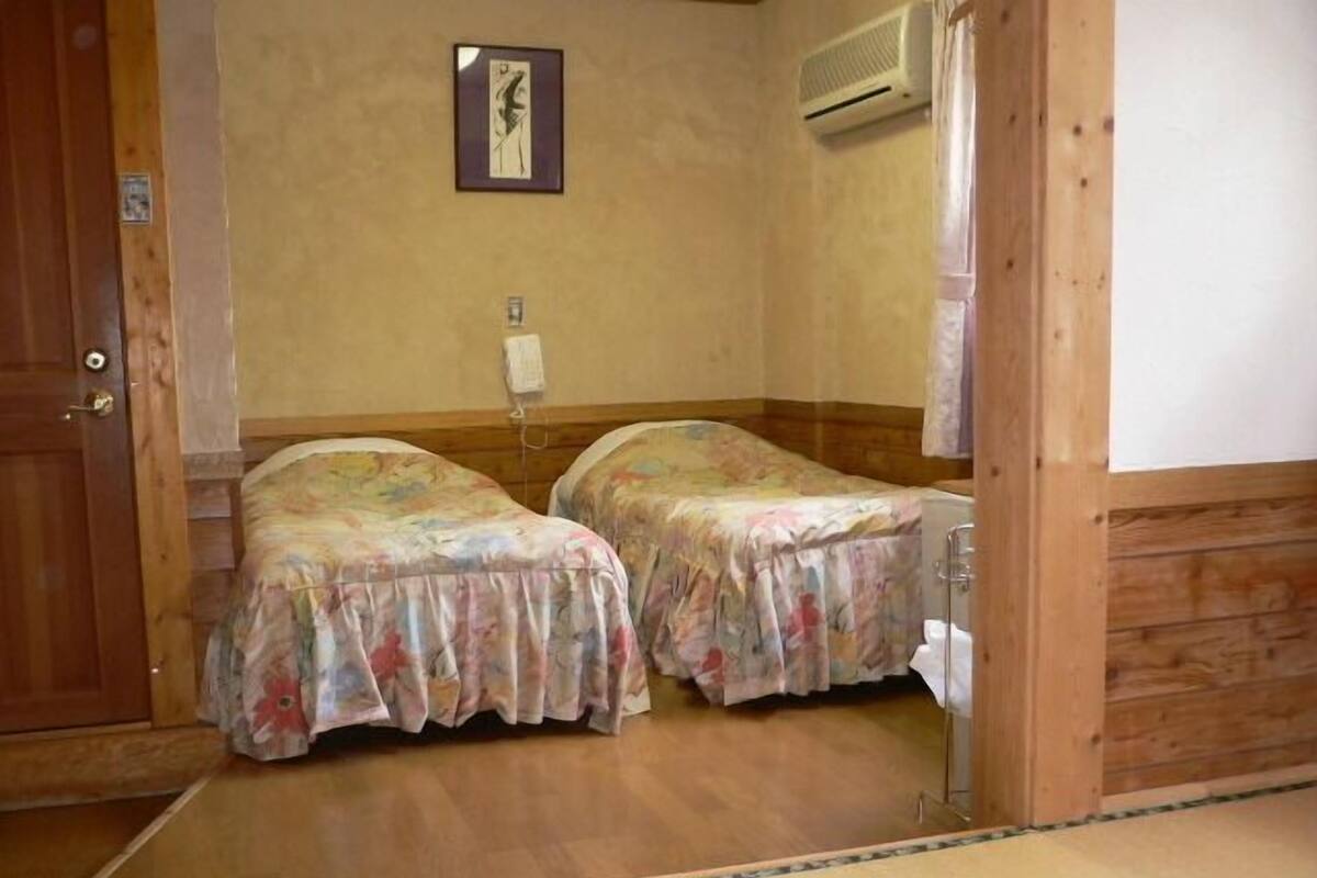 Ein Zimmer mit zwei Betten, Holzboden, einer Wandklimaanlage und einem gerahmten Bild.
