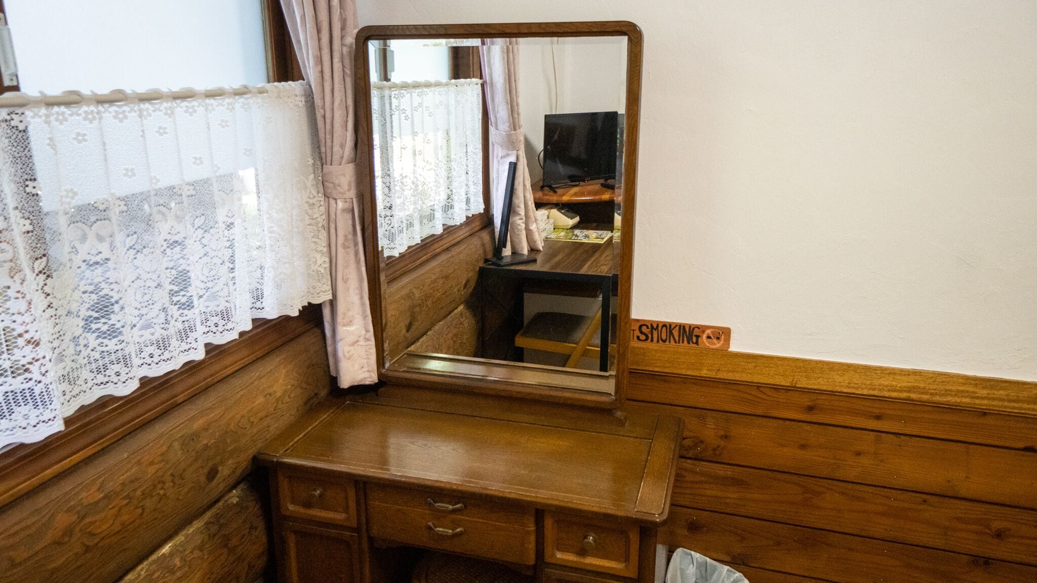 A wooden dresser with a mirror, lace curtains, and a "No Smoking" sign.