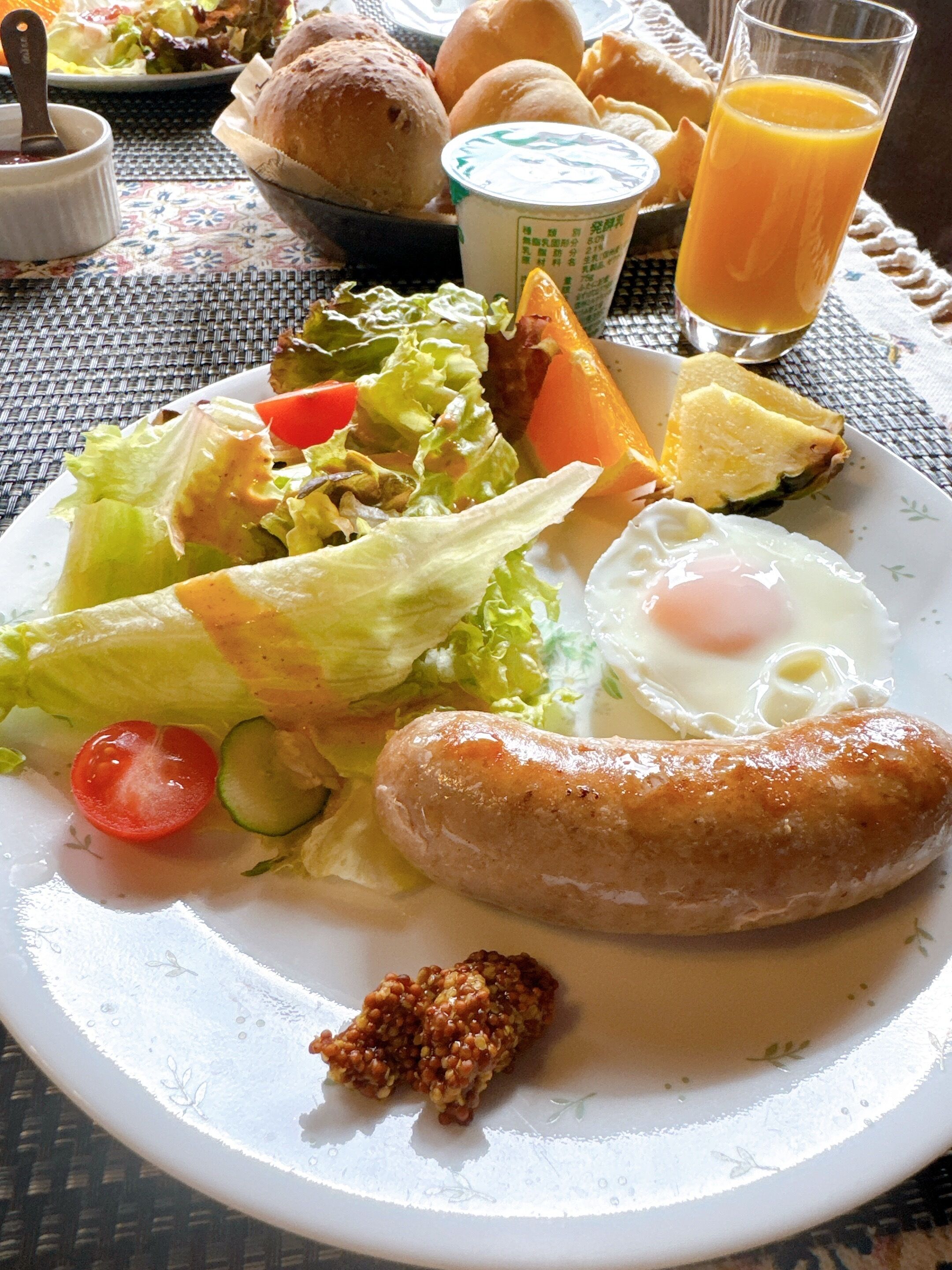 Ein Teller mit einer Wurst, einem Spiegelei, Salat und Brötchen.
