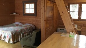 Een houten kamer met een bed, een stoel, een tafel en een raam.