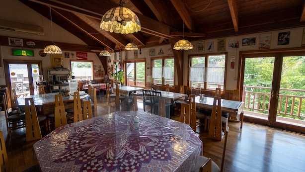 Een restaurant met houten inrichting, grote ramen en een centrale tafel met een tafelkleed met patroon.