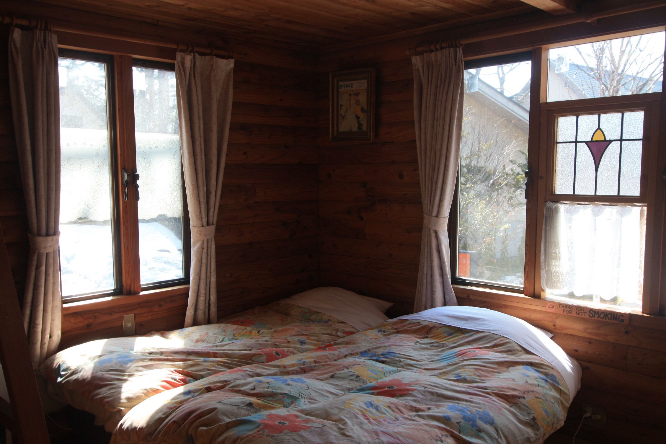 Quarto de cabana acolhedor com cama, paredes de madeira e janelas amplas com cortinas.