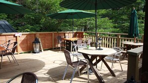 Een terras buiten met houten tafels en stoelen, groene parasols en een houten vlonder.