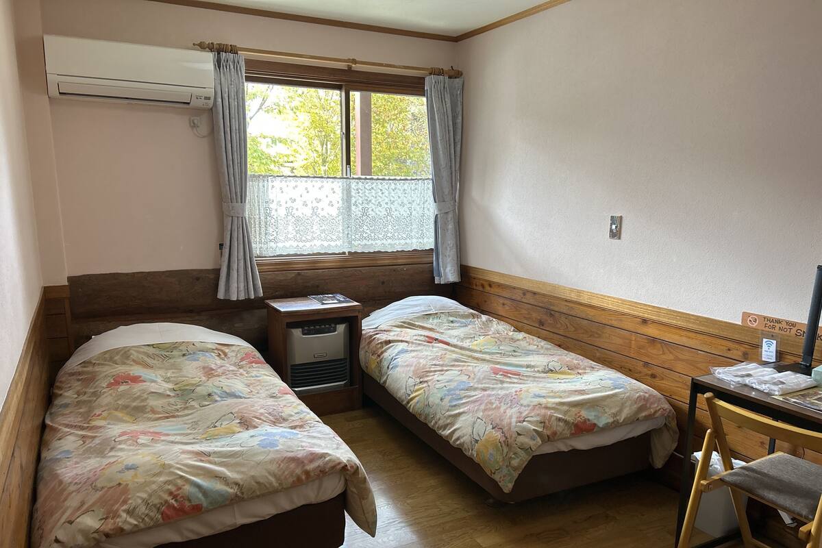 Ein Zimmer mit zwei Betten, einem Schreibtisch, einem Stuhl und einem Fenster mit Vorhängen.