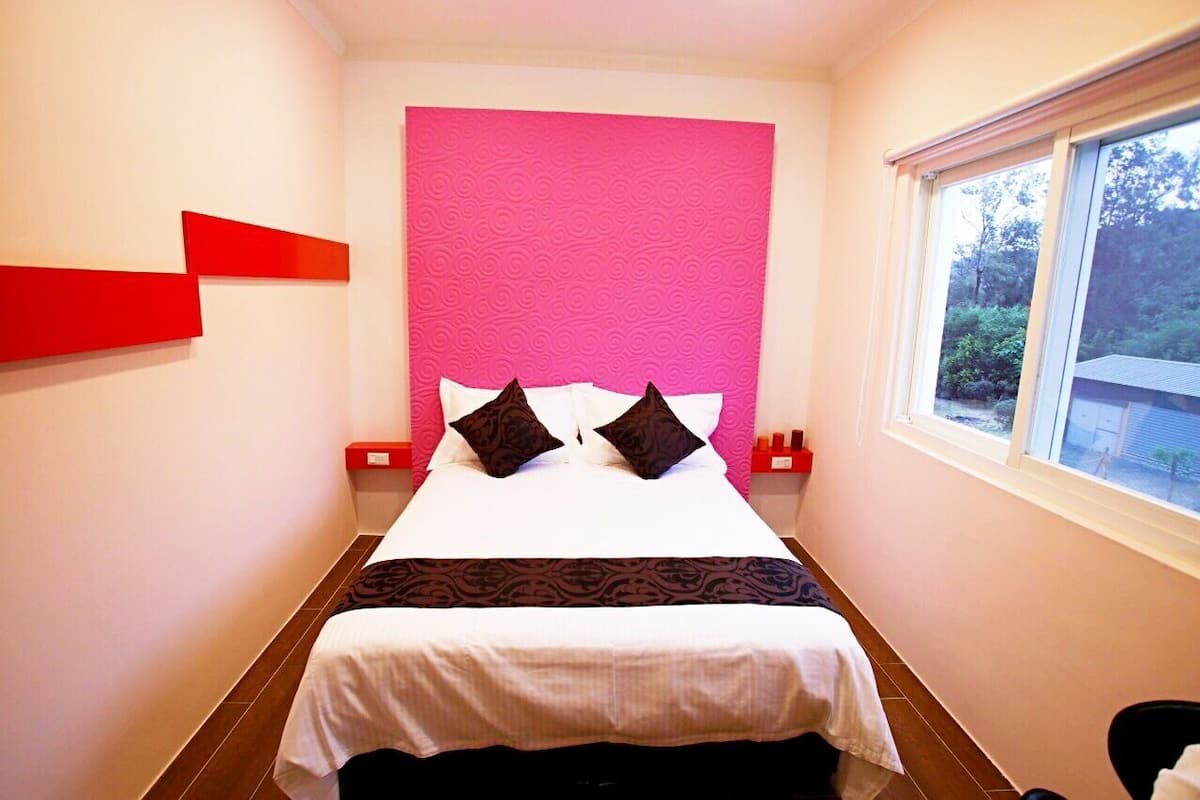 Habitación de hotel con cama, ventana y pared de acento color rosa.